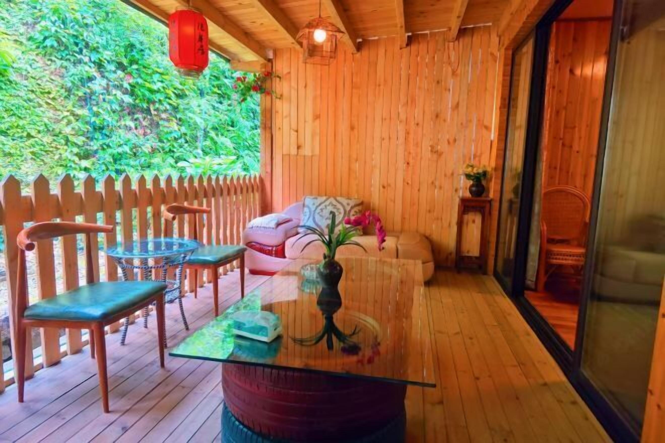 A wooden deck with a glass table and chairs, a cushioned bench, and a red lantern.