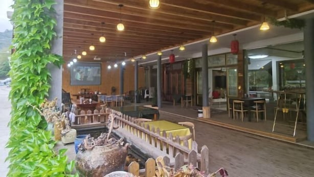 An outdoor dining area with wooden beams, hanging lights, and a rustic wooden fence.