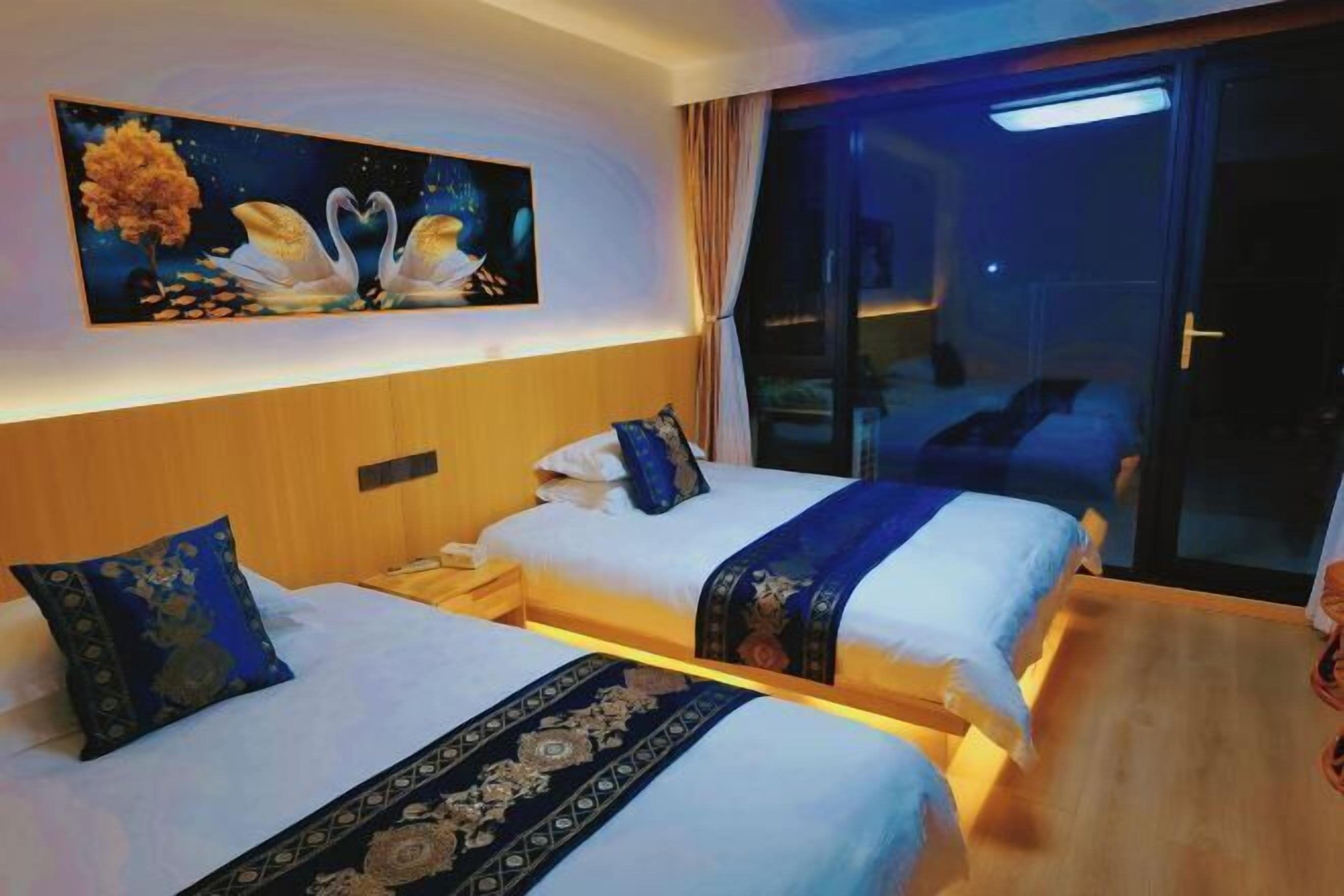 A hotel room with two beds, a nightstand, a painting of swans, and a view of the outside.
