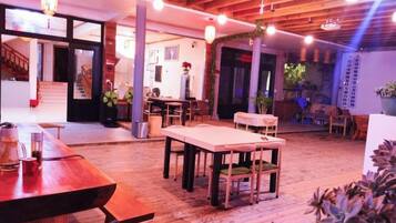 An indoor space with wooden flooring, tables, chairs, and hanging lights.