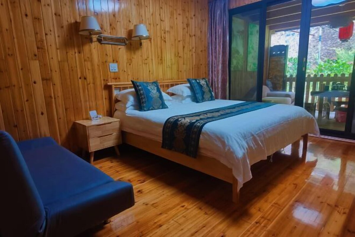 Een kamer met houten lambrisering, een bed, bedlampen en een uitzicht door een glazen deur.