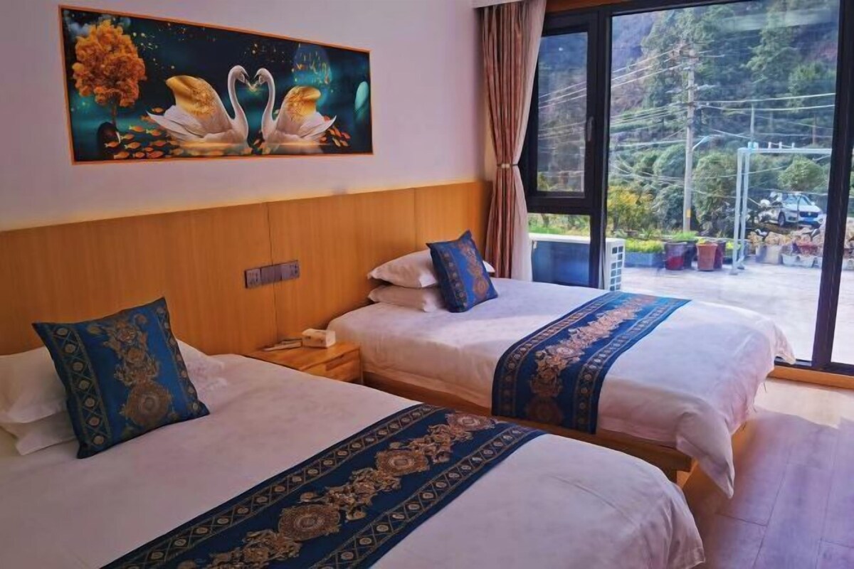 A hotel room with two beds, a painting of swans, and a view of a mountainous area.