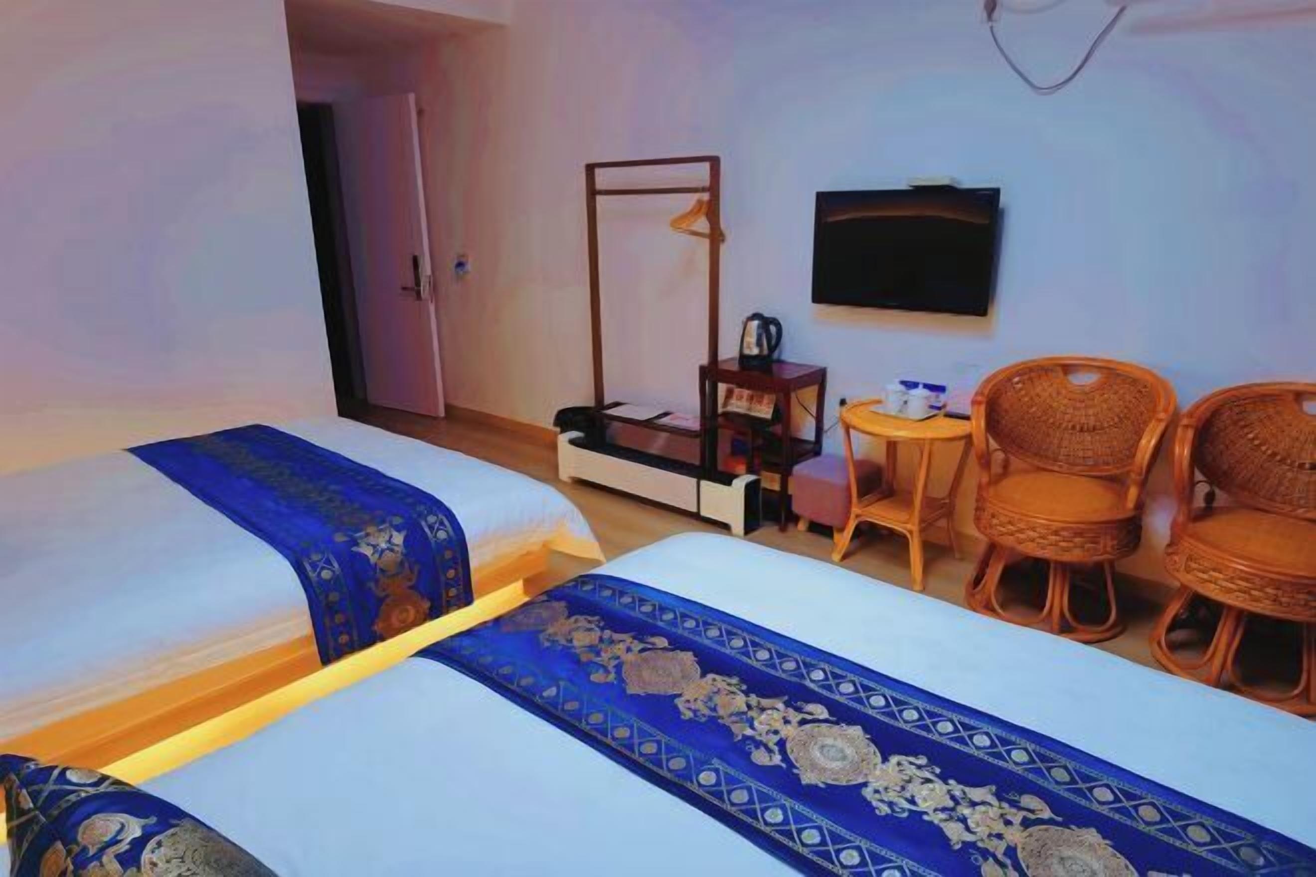 Ein Hotelzimmer mit zwei Betten, einem Fernseher, einem kleinen Tisch und Korbstühlen.