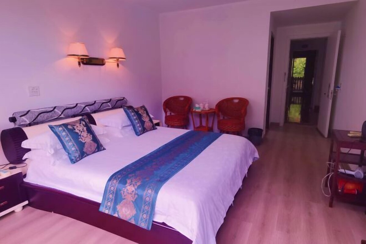 Hotelkamer met een groot bed, twee wandlampen, een kleintje tafeltje met stoelen en een deur naar een balkon.