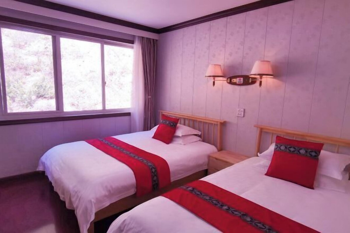 Een hotelkamer met twee bedden, elk met een rood-witte spreideken en passende kussens. Twee wandlampen zijn aan de muur boven de bedden bevestigd.