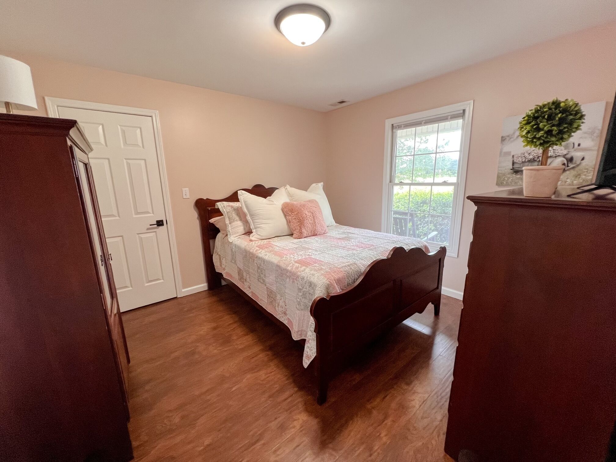 A bedroom with a wooden bed, a door, a window, and a small plant.