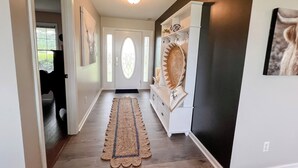 A hallway with a wooden floor, a rug, a white console table with decorative items, and a black accent wall. - Peaceful - View - Close to Owensboro - Modern Farmhouse (Utica)