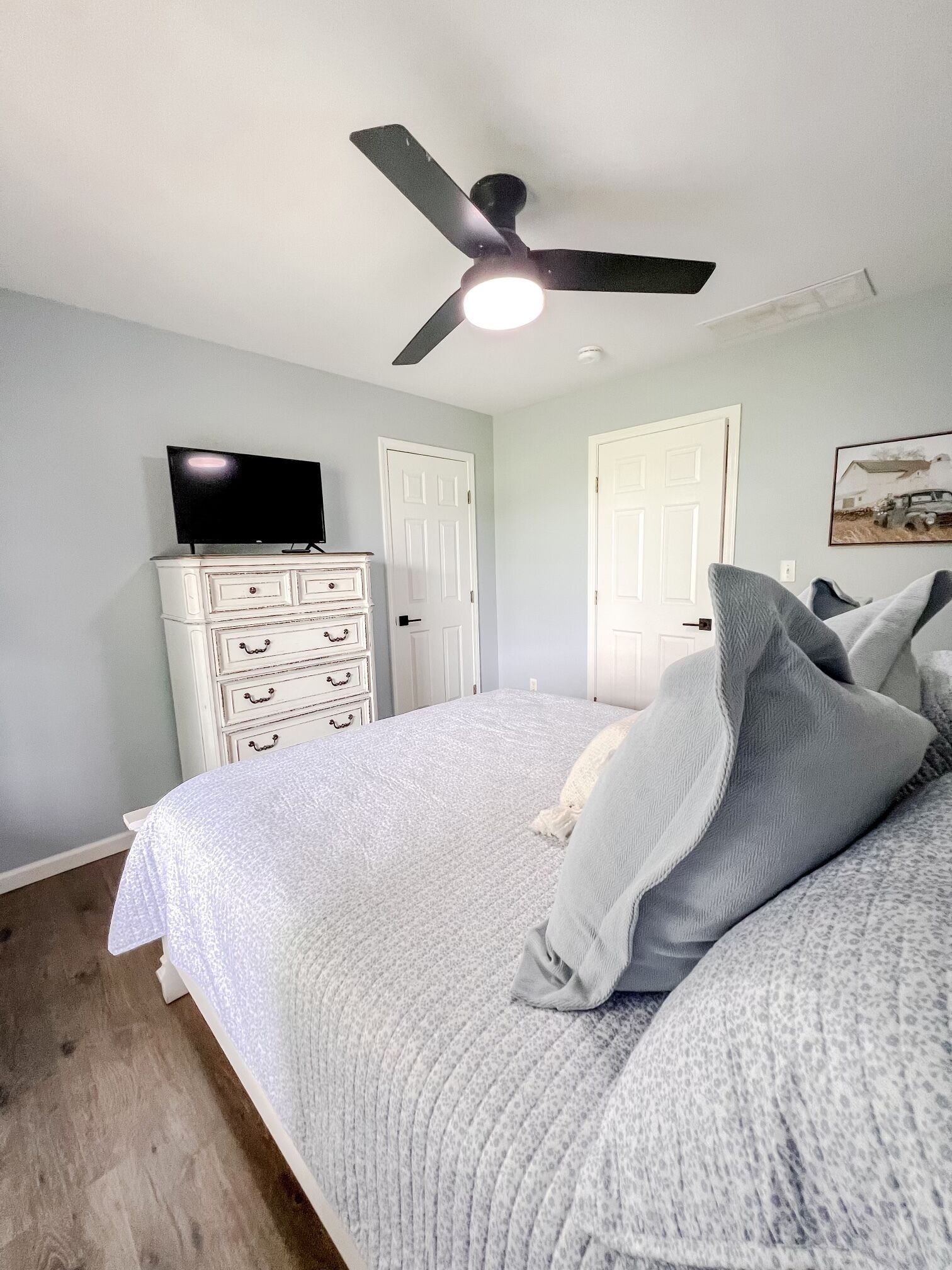 Un dormitorio con cama, ventilador de techo, cómoda y televisor encima.