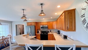 A modern kitchen with wooden cabinets, a large island with bar stools, stainless steel appliances, and a wall clock. - Peaceful - View - Close to Owensboro - Modern Farmhouse (Utica)