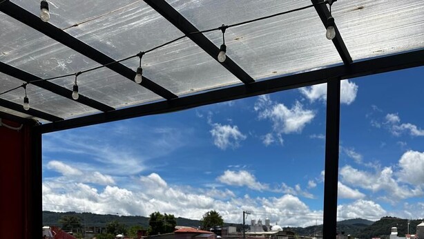 An outdoor patio with a glass table, a teal chair, and potted plants. - VOE HOTEL (San Cristóbal de las Casas)