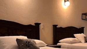 A hotel room with two beds, each with a headboard, a blue blanket, and wall-mounted light fixtures. - VOE HOTEL (San Cristóbal de las Casas)