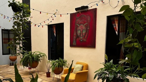 A courtyard with potted plants, a yellow chair, and a red painting on the wall. - VOE HOTEL (San Cristóbal de las Casas)
