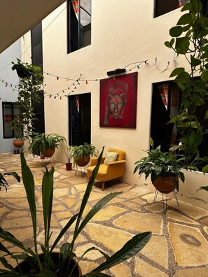 Une cour avec des plantes en pot, une chaise jaune et un tableau rouge accroché au mur.