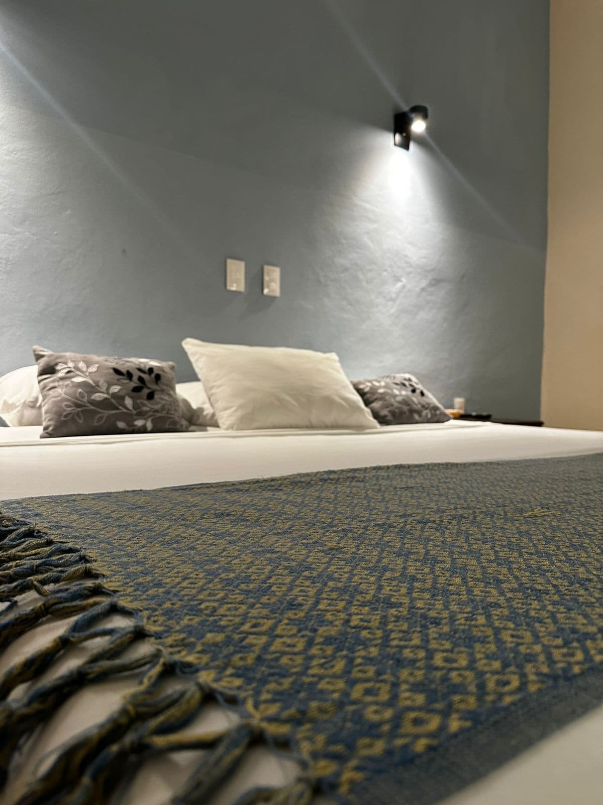 A bed with a patterned rug, a wall-mounted light, and two wall sconces.