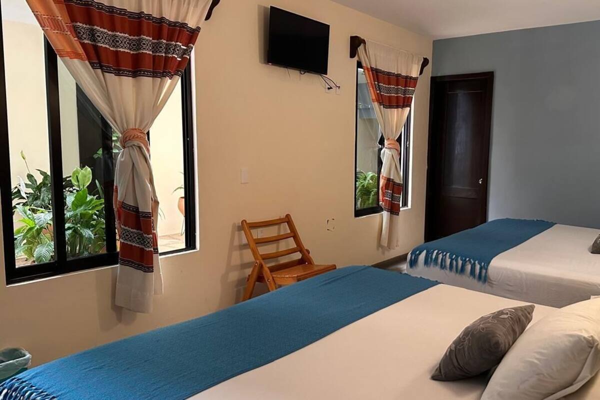 Habitación de hotel con dos camas, televisión, una silla de madera y cortinas.