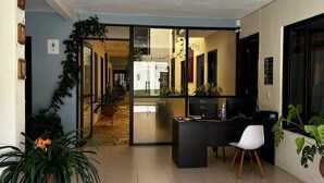 A hotel lobby with a reception desk, a seating area, and a glass door leading to a hallway. - VOE HOTEL (San Cristóbal de las Casas)