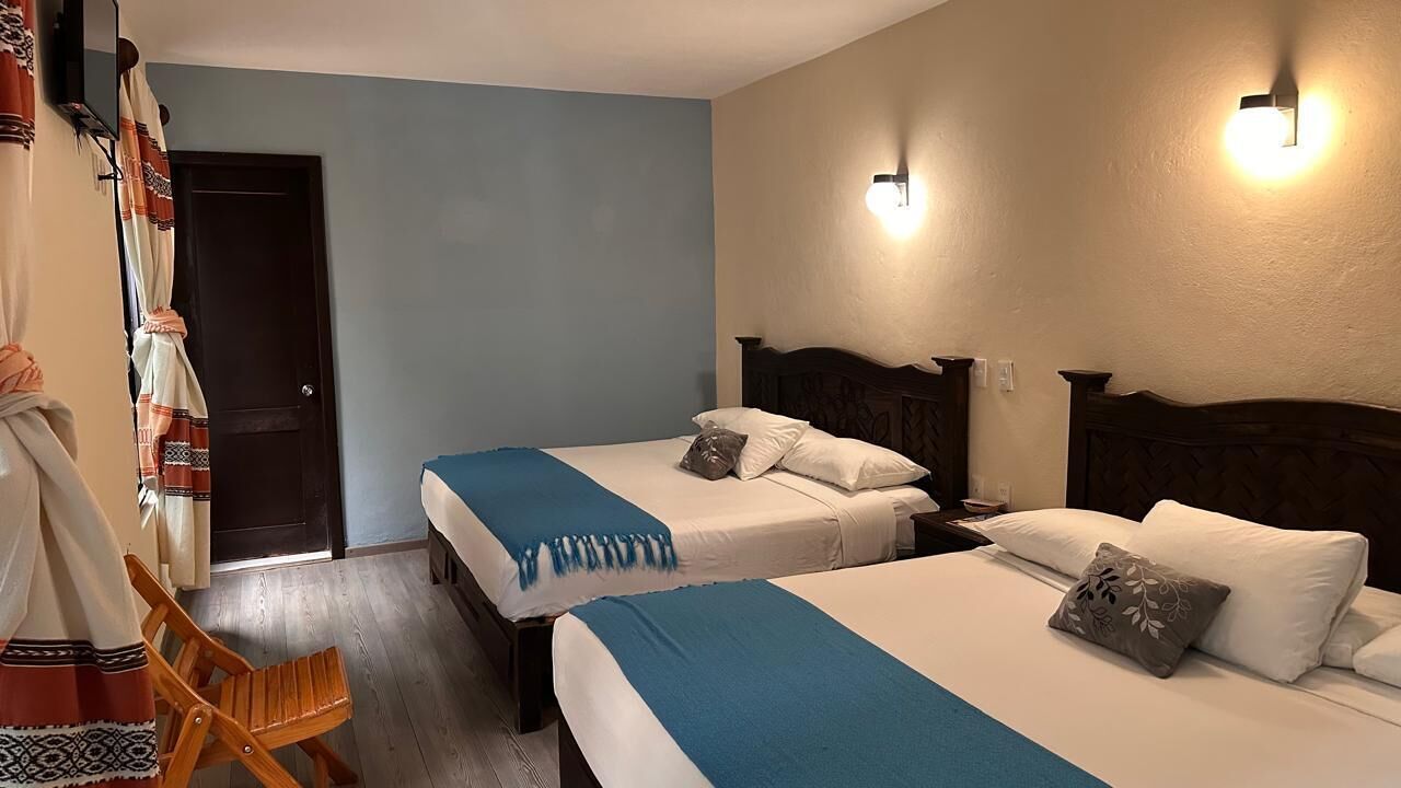 Une chambre d’hôtel avec deux lits, une chaise en bois, une porte et des lampes fixées au mur.