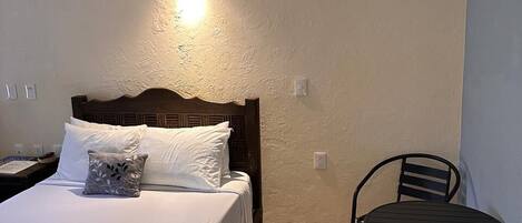 A bedroom with a bed, bedside table, lamp, and a small table with chairs.