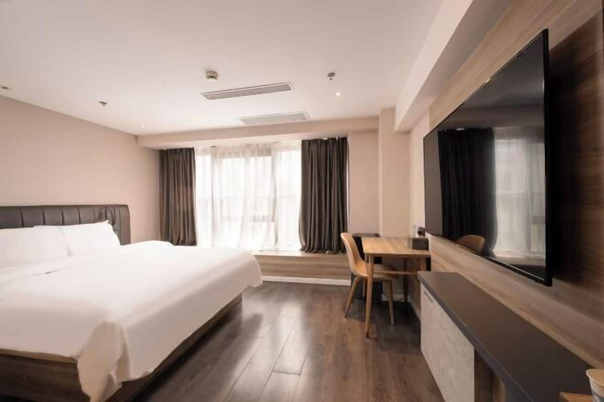 Habitación de hotel con cama, escritorio, silla, televisor y ventana con cortinas.