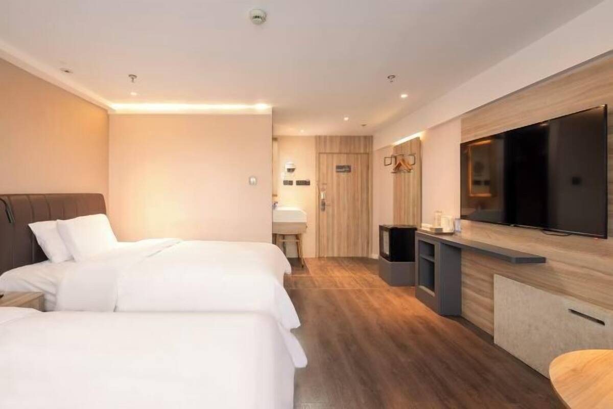 Habitación de hotel con dos camas, televisión, kitchenette pequeña y baño.