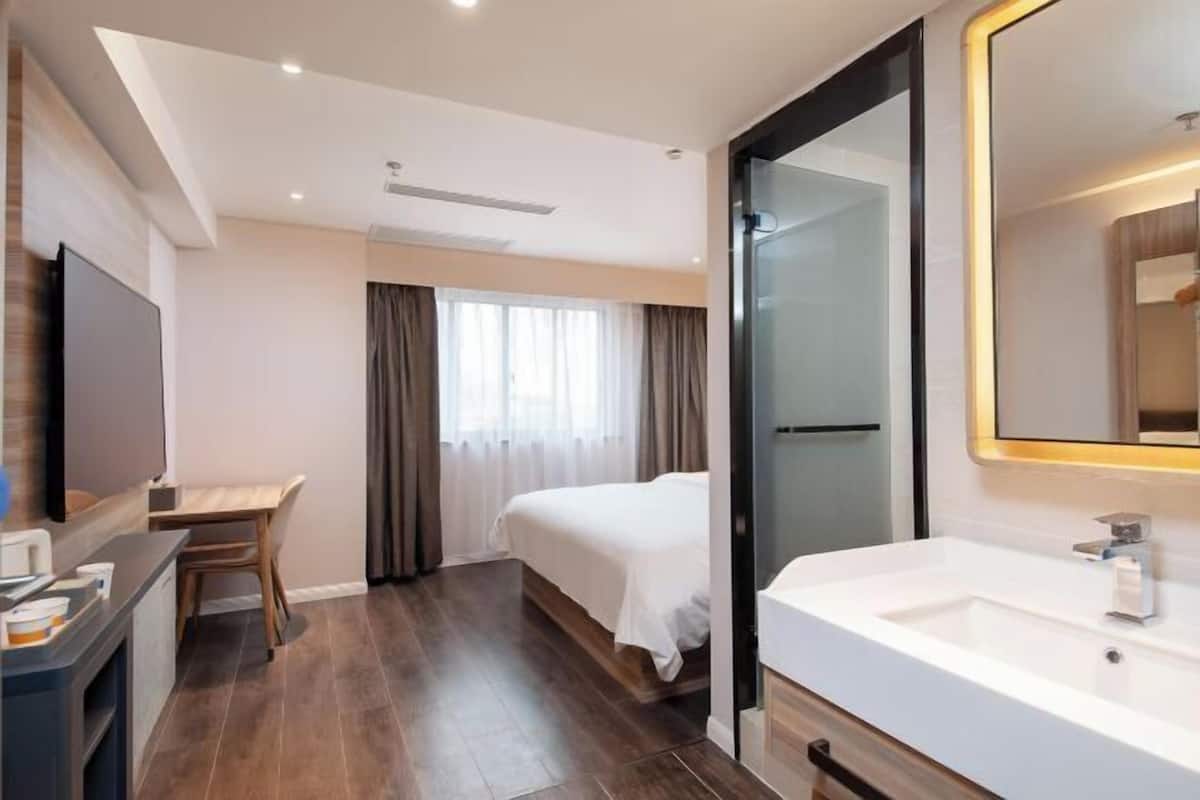 Habitación de hotel con cama, escritorio, televisor y baño con lavamanos y un espejo grande.