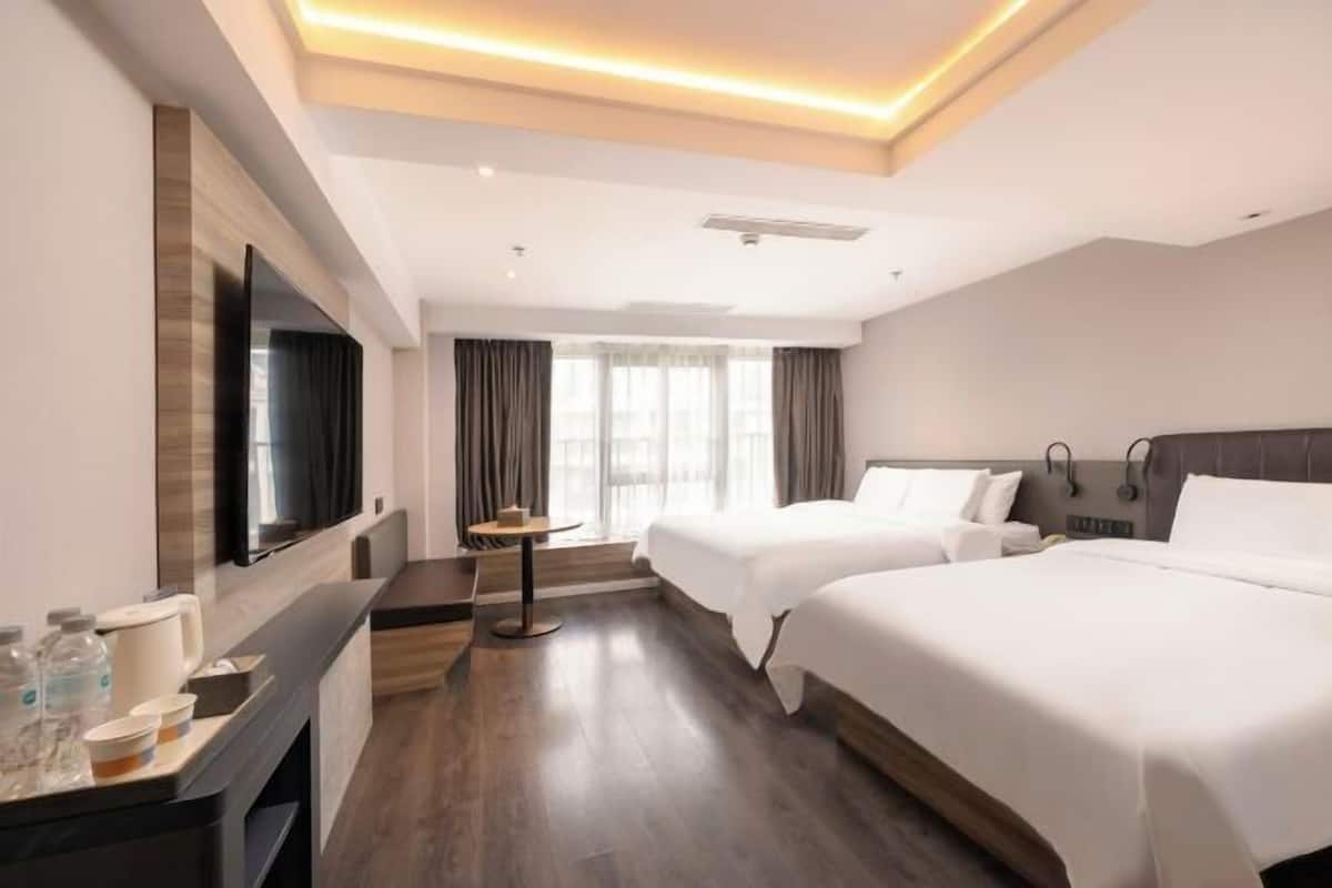 Habitación de hotel con televisión, dos camas, escritorio con cafetera y una mesita.