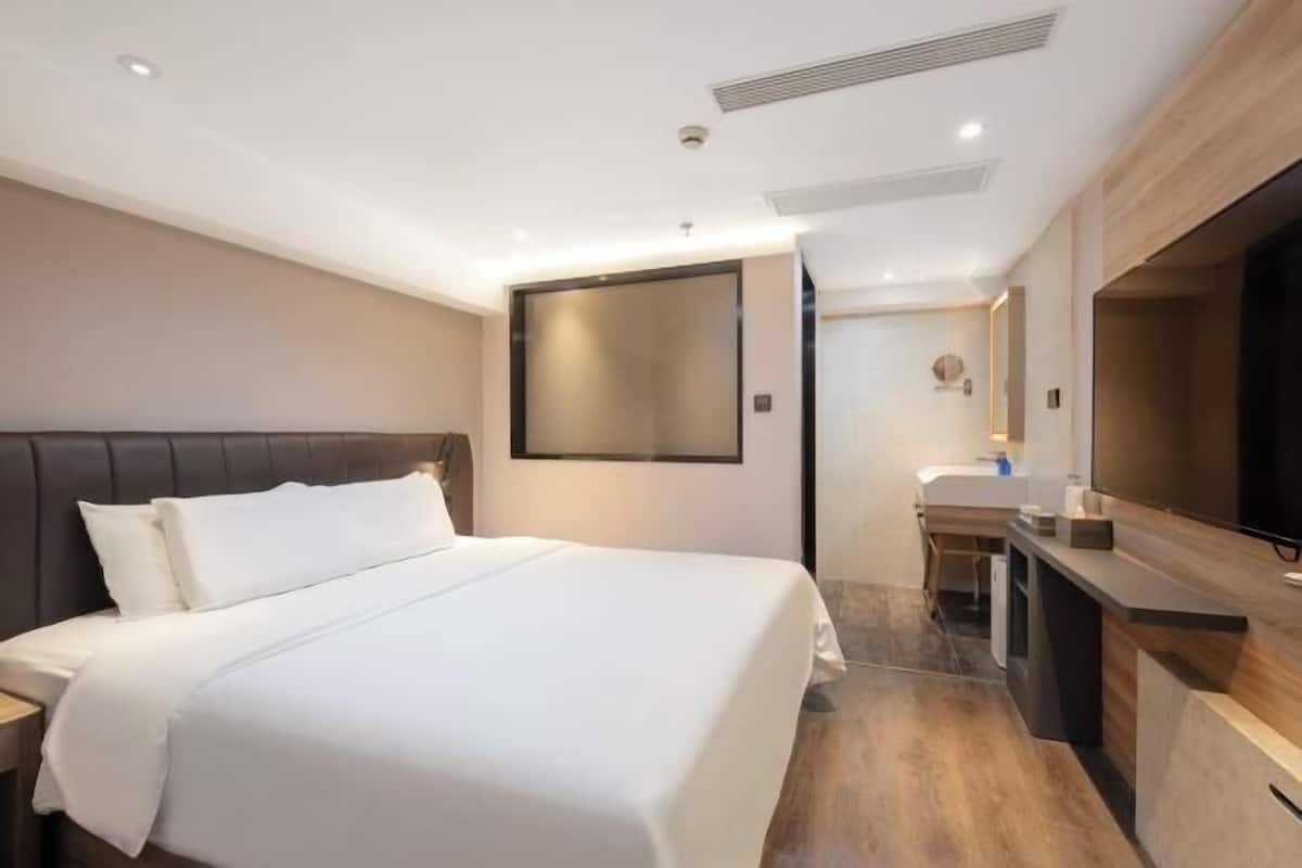 Habitación de hotel con una cama grande, un escritorio con televisor de pantalla plana, un espejo y una pequeña kitchenette.