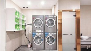 A laundry area with two stacked washing machines, a drying rack, and shelves with green bottles. - HanTing Premium Hotel (Shanghai Pudong Airport Chenyang Road) (Shanghai)