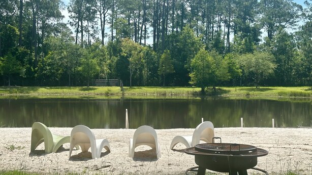 A lakeside seating area with white chairs and a fire pit.
