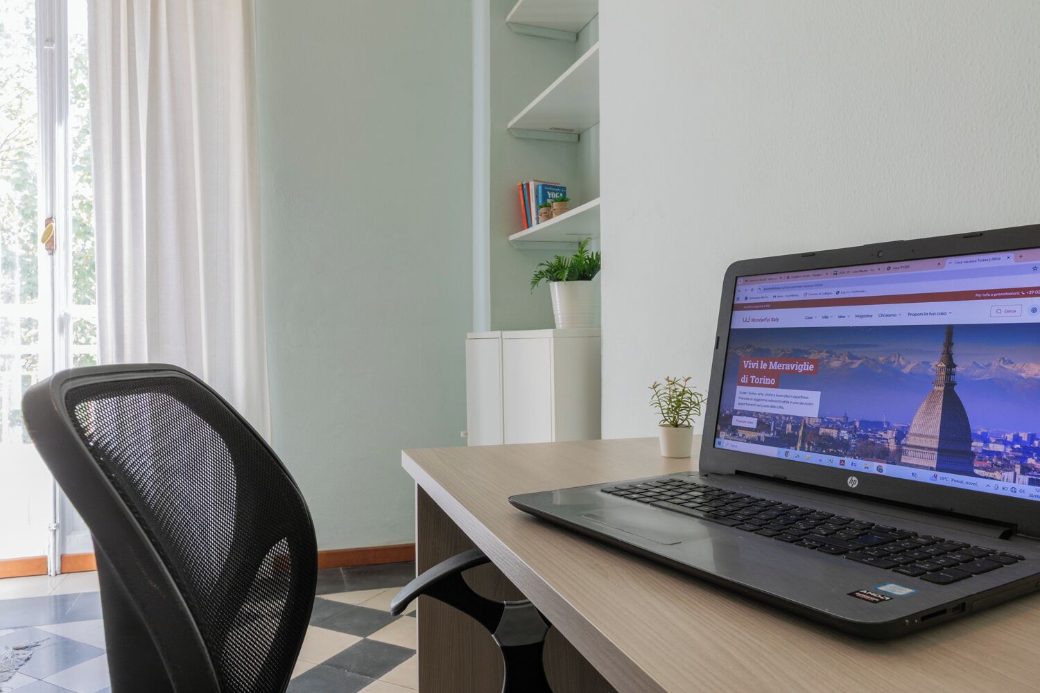 A laptop on a desk with a view of a cityscape on the screen, a chair, a plant, and a bookshelf in the background.