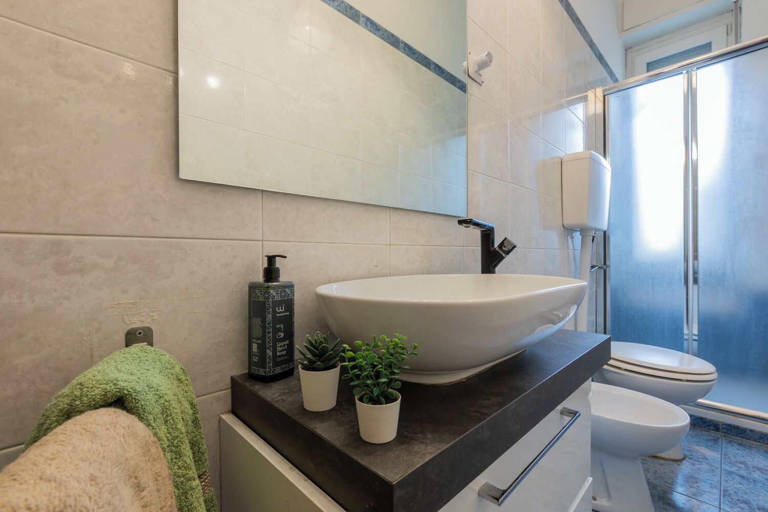 A modern bathroom with a large vessel sink, a handheld showerhead, a toilet, and a towel rack.