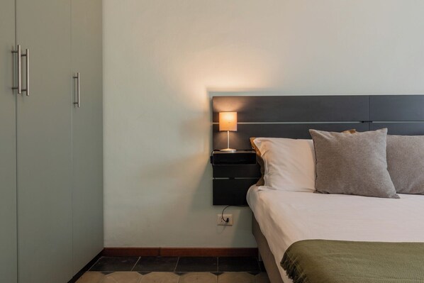 Una habitación de hotel con una cama, una mesita de noche con lámpara y un armario.