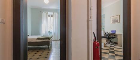 Una habitación de hotel con una cama, un escritorio con una computadora, un extintor y un piso a cuadros.