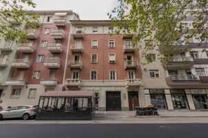 Un edificio residenziale a più piani con balconi, un negozio e un'auto parcheggiata.
