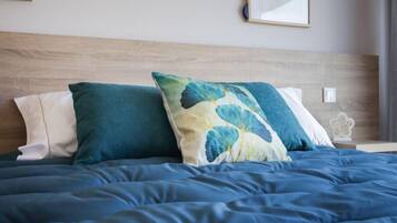A neatly made bed with a blue comforter and two pillows, one with a floral pattern and the other plain.