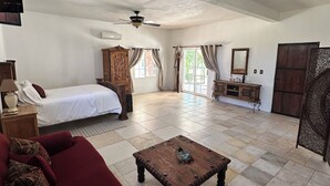 A spacious living area with a large sofa, a wooden coffee table, a ceiling fan, and a bed with curtains. - Casa Luna Viñedo (Valle de Guadalupe)