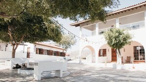 A courtyard with a white bench, trees, and a building with arches and a balcony. - Casa Luna Viñedo (Valle de Guadalupe)
