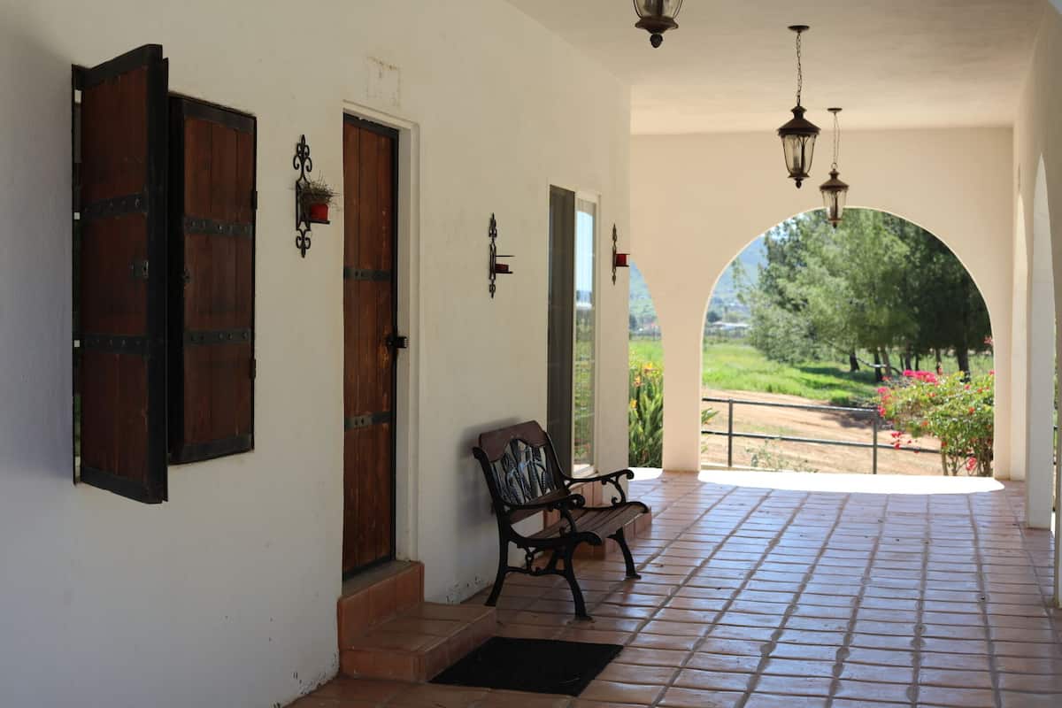 A covered porch with a bench, a wooden door, and a view of greenery.