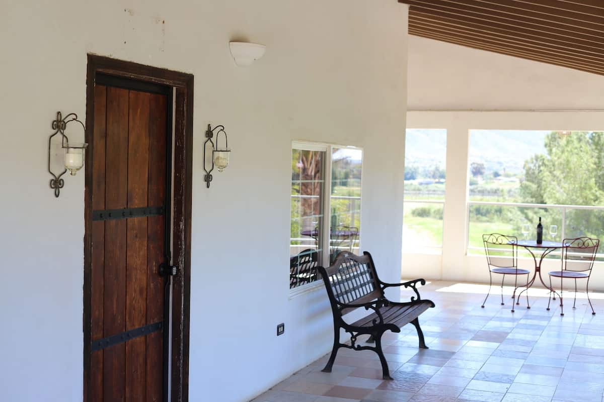 A room with a wooden door, a bench, a table with chairs, and a view of the outdoors.