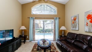 A living room with a TV, leather sofa, coffee table, and artwork on the walls. - Beautiful 4 Bedroom Villa near Disney World with Private Pool (Kissimmee)