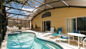 A covered outdoor swimming pool with lounge chairs and a table, surrounded by a glass enclosure. - Beautiful 4 Bedroom Villa near Disney World with Private Pool (Kissimmee)