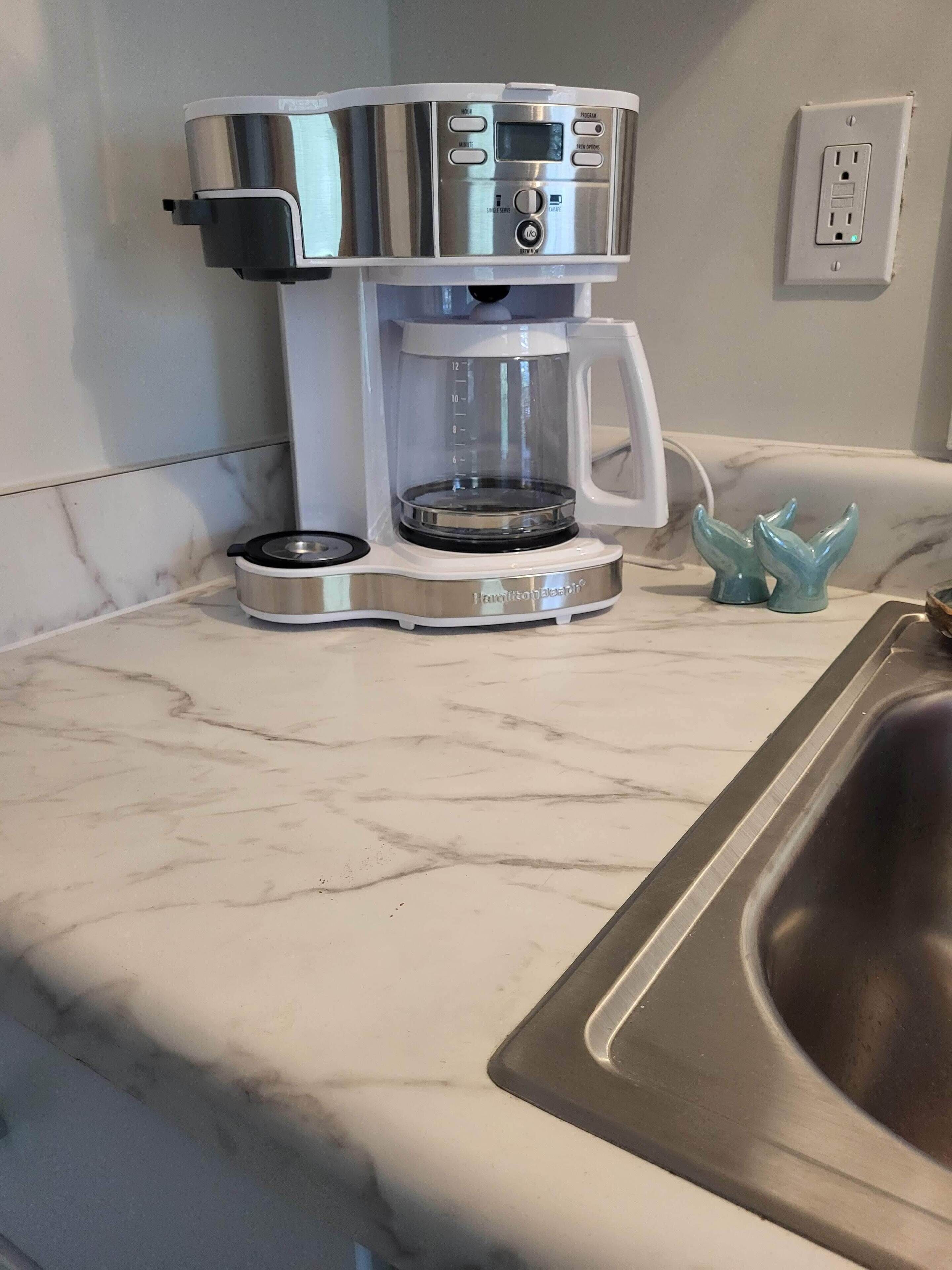 A kitchen with a coffee maker, a sink, and a marble countertop.