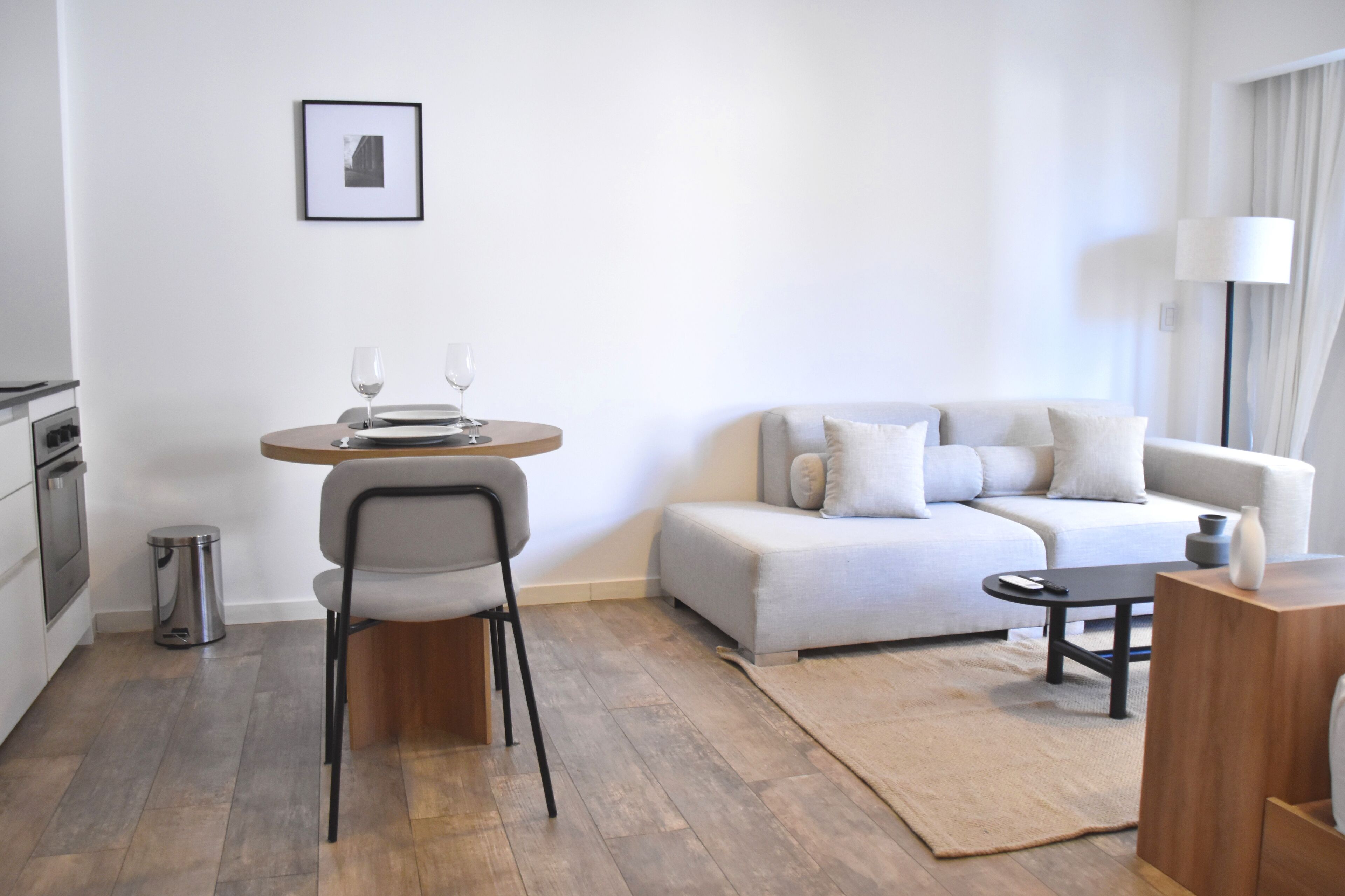 Ein modernes Wohnzimmer mit Sofa, Esstisch mit Stühlen, einer kleinen Küchenzeile und einem gerahmten Bild an der Wand.