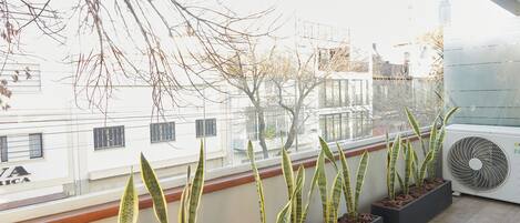 A balcony with potted plants, a window, and an air conditioning unit.