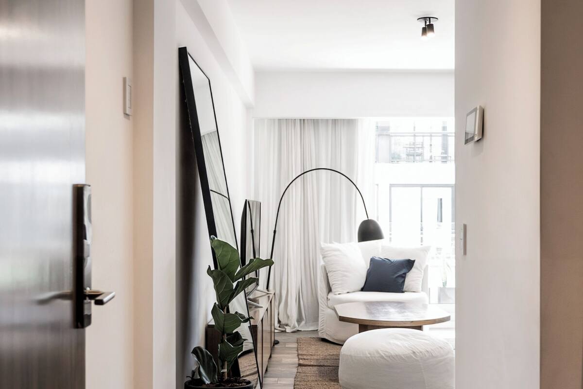 A narrow hallway with a potted plant, a white sofa with a blue pillow, and a floor lamp.