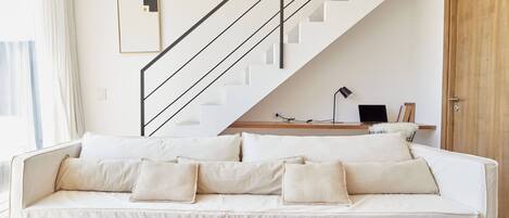 Una sala de estar moderna con un sofá blanco, una mesa de centro de madera, una escalera con barandilla negra y una puerta de madera.