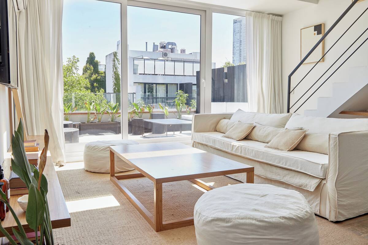 A modern living room with a sofa, coffee table, and a view of the city through large windows.
