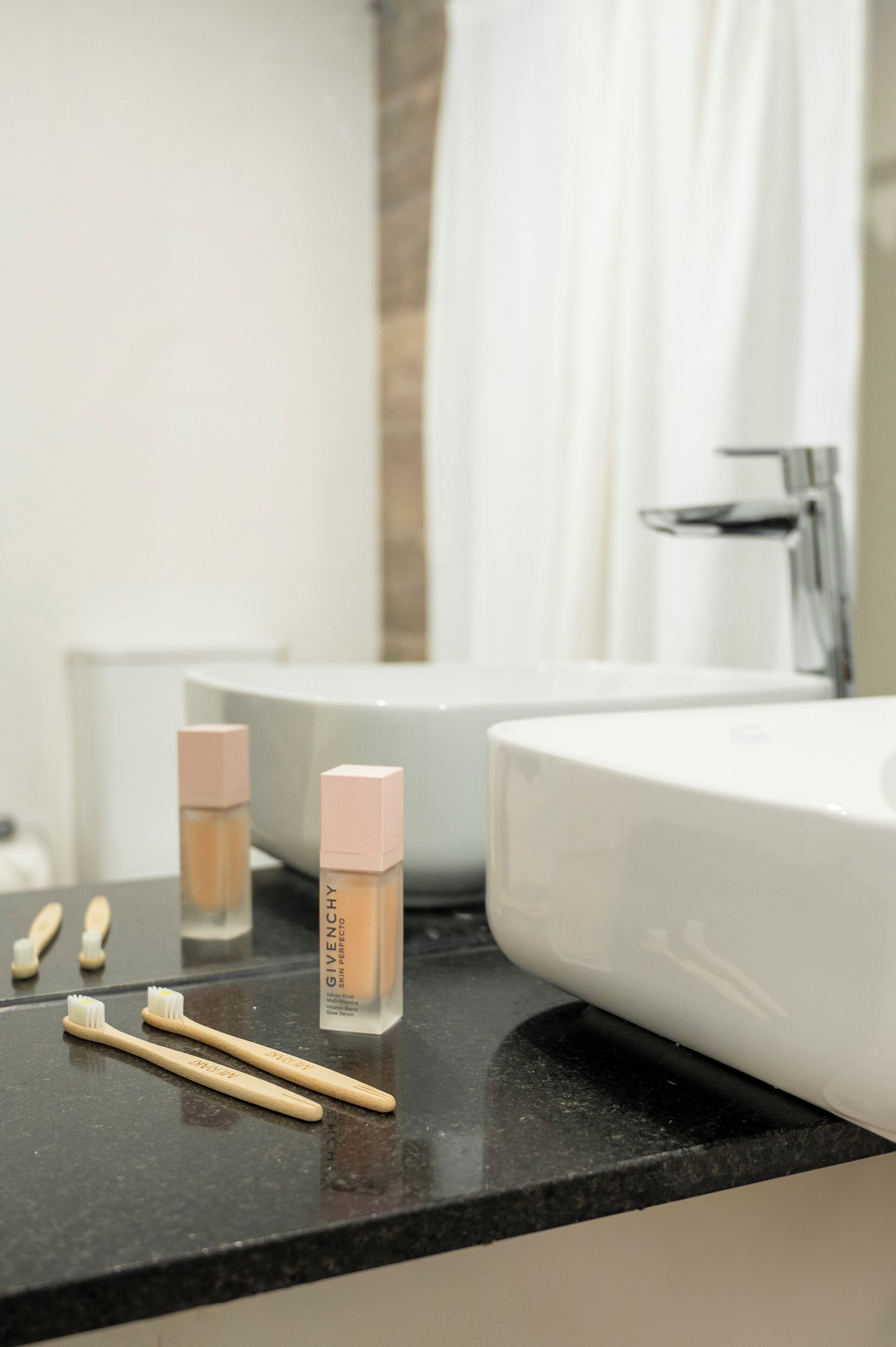 A bathroom counter with a white sink, a bottle of foundation, and two toothbrushes.