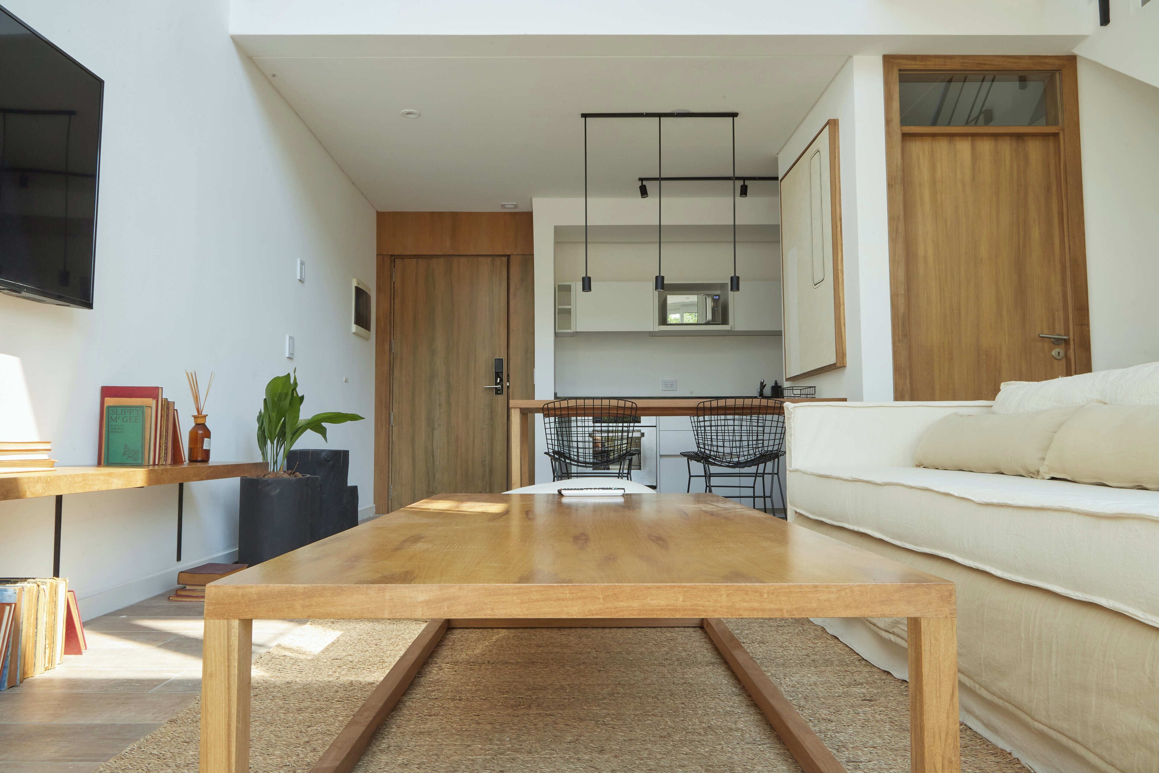 Un salon moderne avec une table basse en bois, un canapé et un coin cuisine équipé d’un four à micro-ondes et de luminaires suspendus.