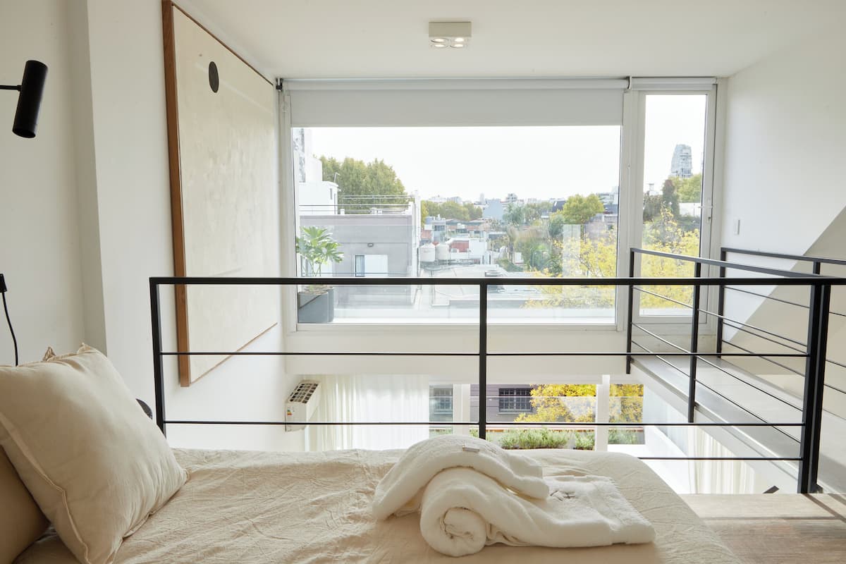 A bedroom with a large window, a bed with rolled towels, and a view of the cityscape.